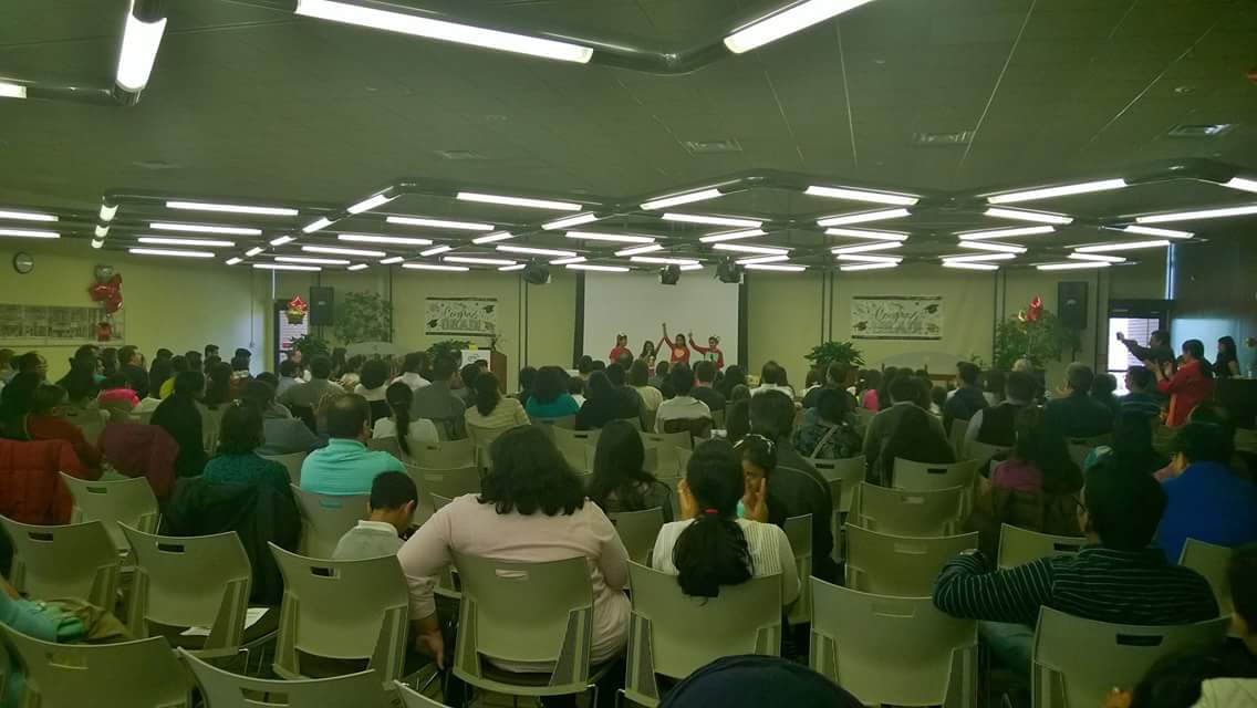 A large hall filled with rows of seated families facing speakers at the front of the room
