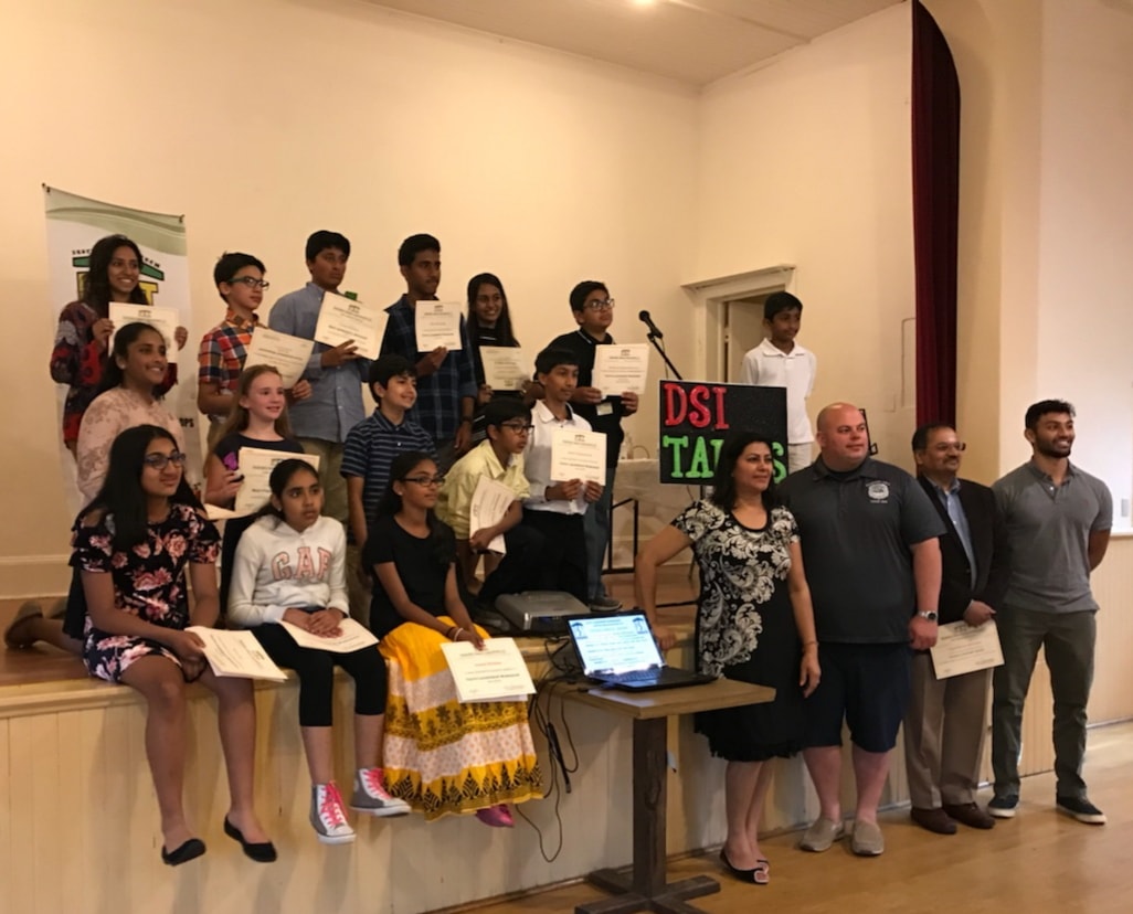 A group of DSI students holding certificates on and around a stage beside a hand-lettered DSI TALKS sign, with guest judges standing to the right