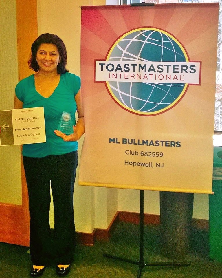 Coach Priya Sundararaman holding her first-place Toastmasters Speech Evaluation Contest certificate and trophy