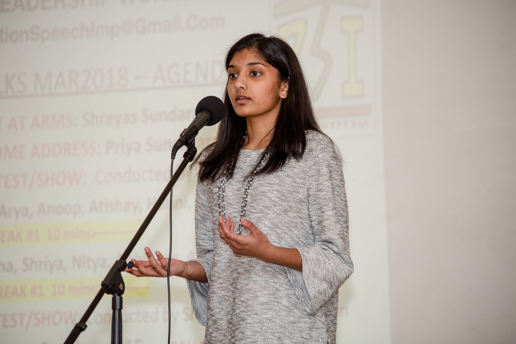 A DSI student mid-speech at the microphone, the DSITalks agenda projected behind her