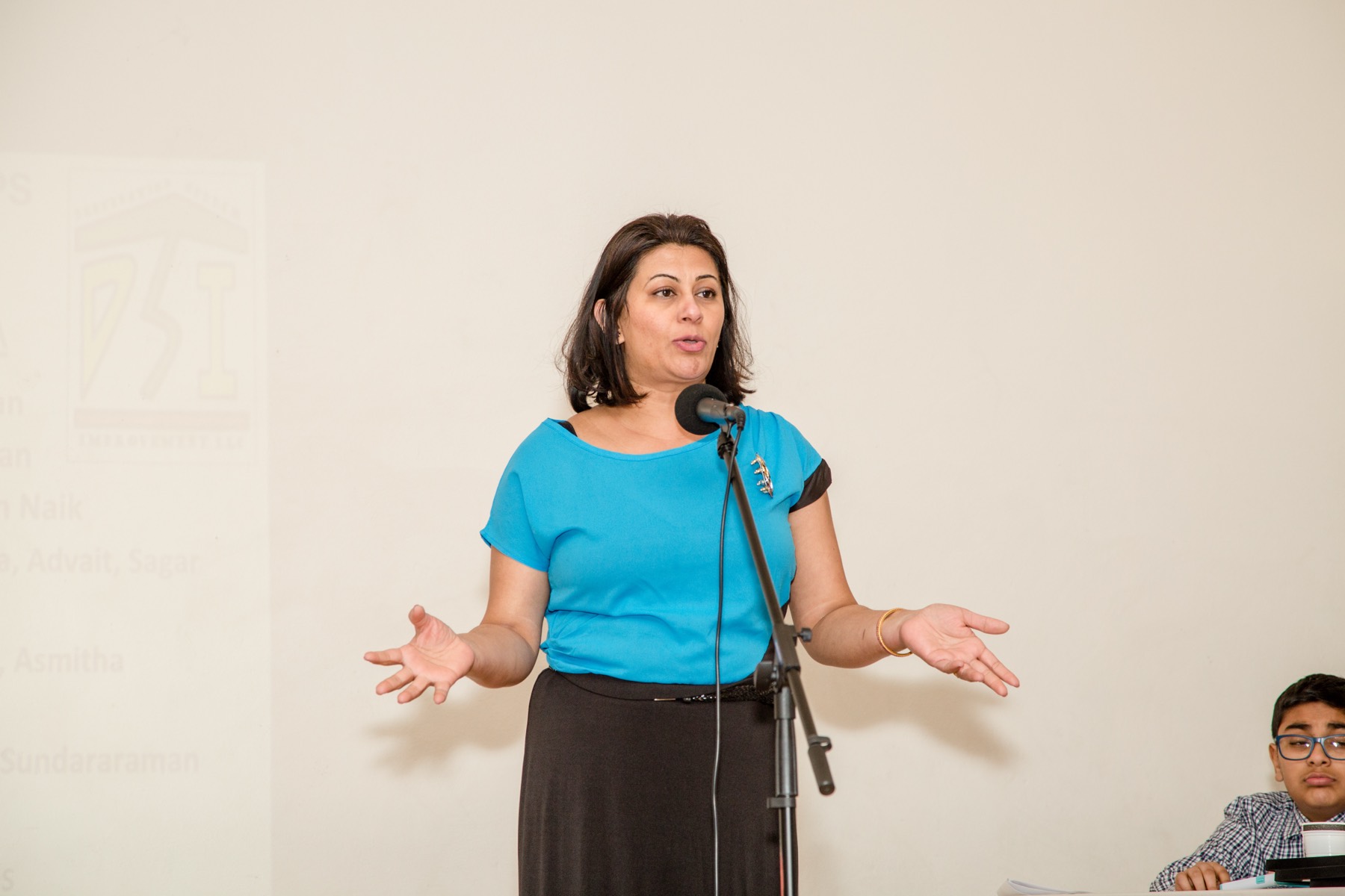 An adult speaker addressing the room at a DSI event, the DSI logo projected behind her