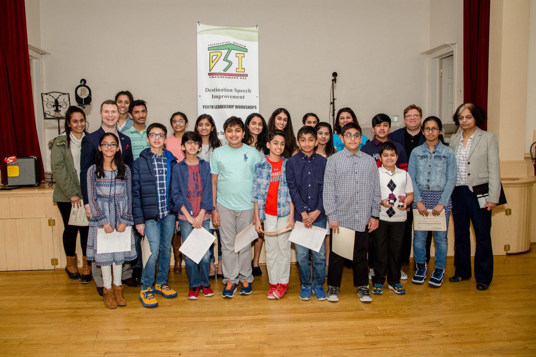 A full DSI cohort with their certificates, standing beneath the Destination Speech Improvement Youth Leadership Workshops banner