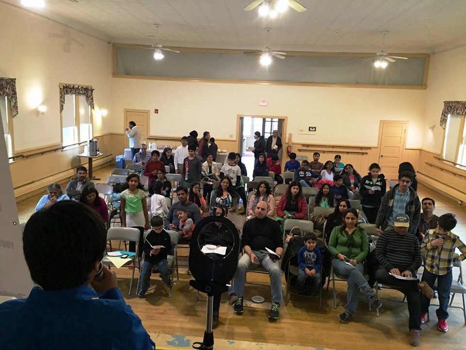 The view from the front of the room at a DSI event — a young speaker facing a hall full of families